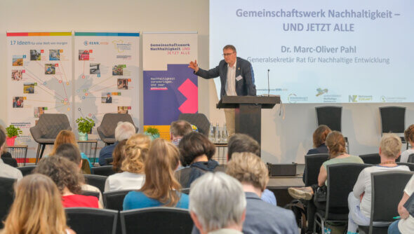 Der Generalsekretär des Rates für Nachhaltige Entwicklung Marc-Oliver Pahl stellt vor Publikum auf einer Bühne das Projekt „Gemeinschaftswerk Nachhaltigkeit" vor. © Ulrich Wessollek, RENN.mitte