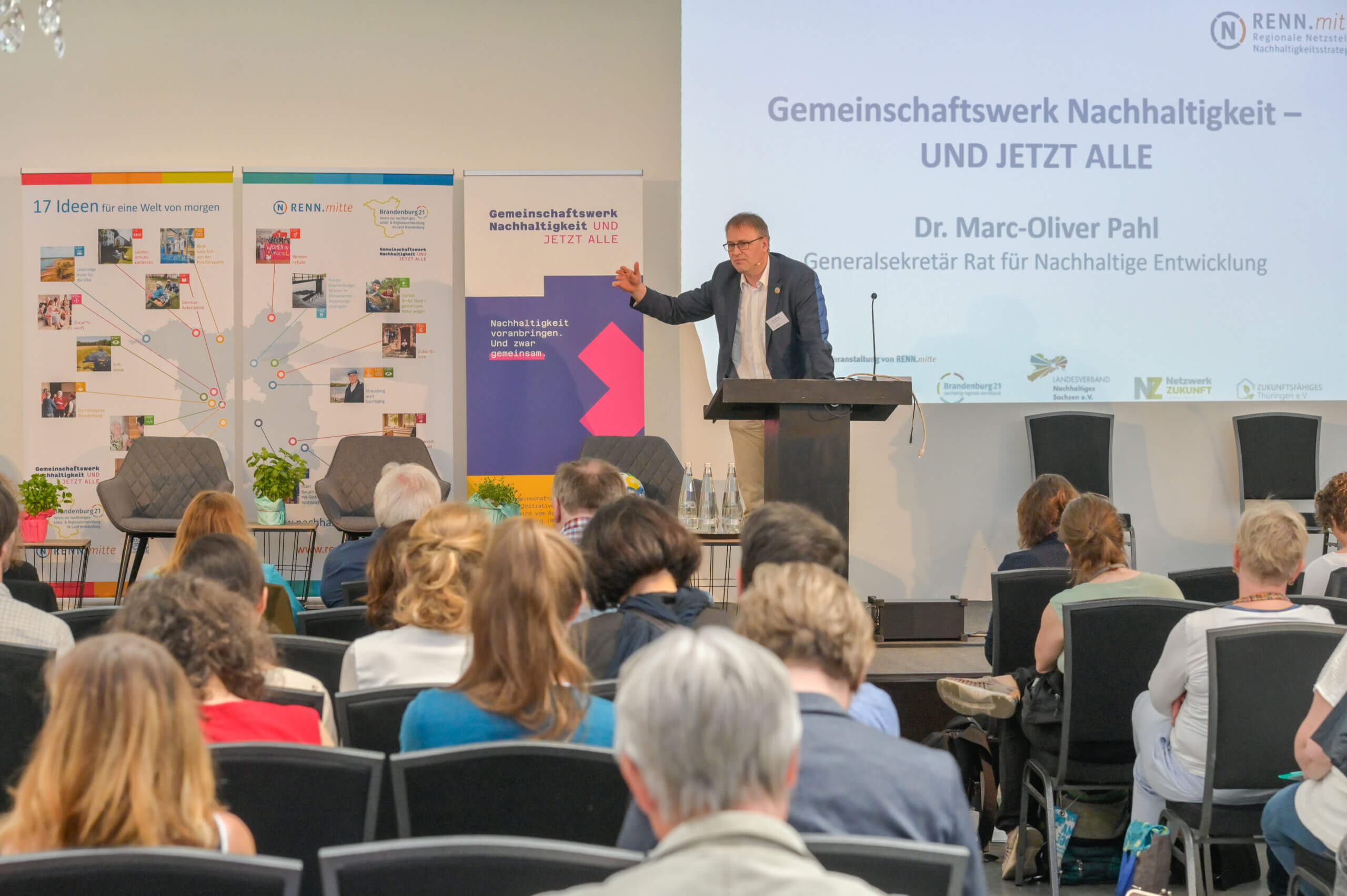 Der Generalsekretär des Rates für Nachhaltige Entwicklung Marc-Oliver Pahl stellt vor Publikum auf einer Bühne das Projekt „Gemeinschaftswerk Nachhaltigkeit" vor. © Ulrich Wessollek, RENN.mitte