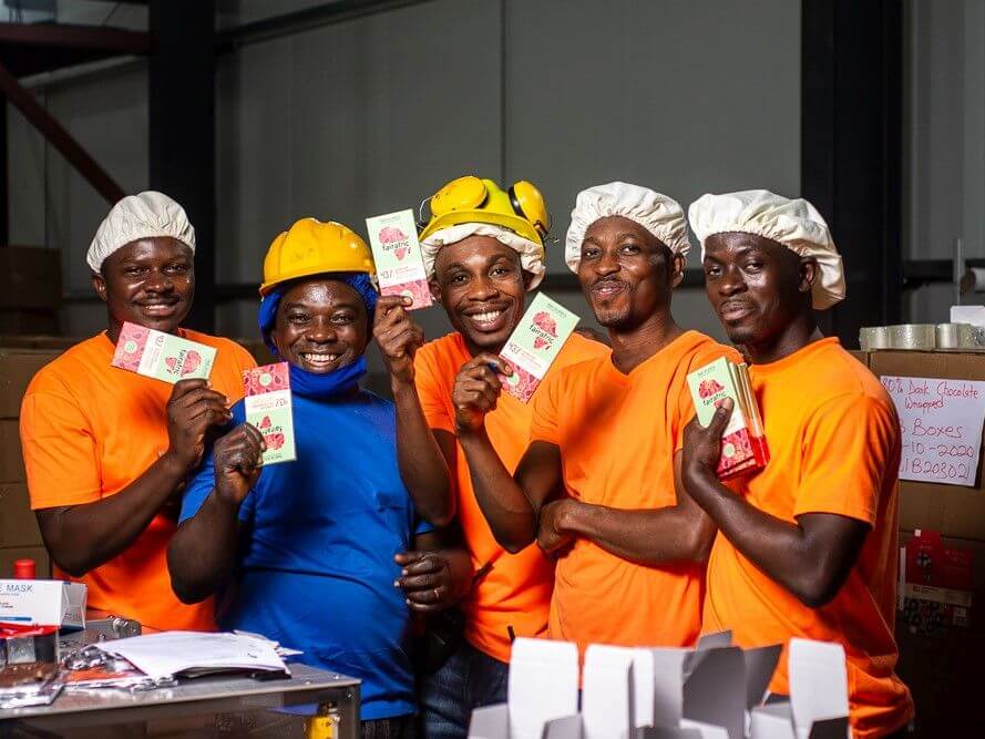 Arbeiter in einer Fabrik in Ghana präsentieren nachhaltig produzierte Schokolade von Fairafric.