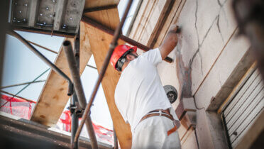 Ein Bauarbeiter steht auf einem Gerüst zur Sanierung eines Gebäudes.