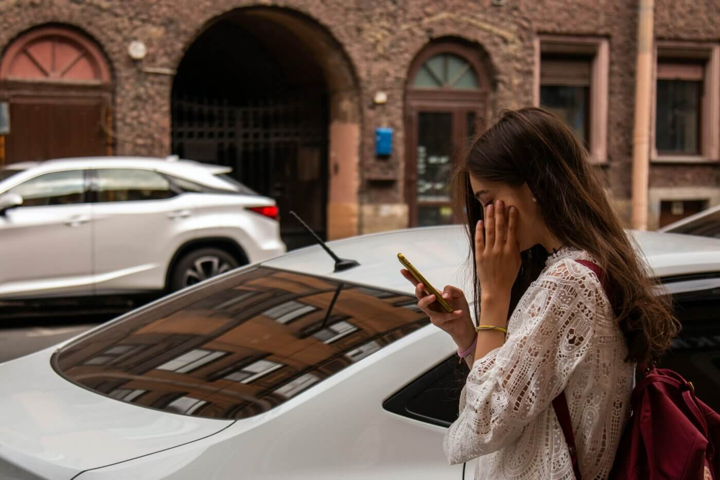 Eine Frau steht an einer Straße vor Autos und schaut auf ein Handy.