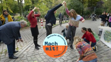 Menschen stehen am Rande eines Parks und ziehen gemeinsam an Bändern. Ein Spiel im Rahmen der Deutschen Aktionstage Nachhaltigkeit.