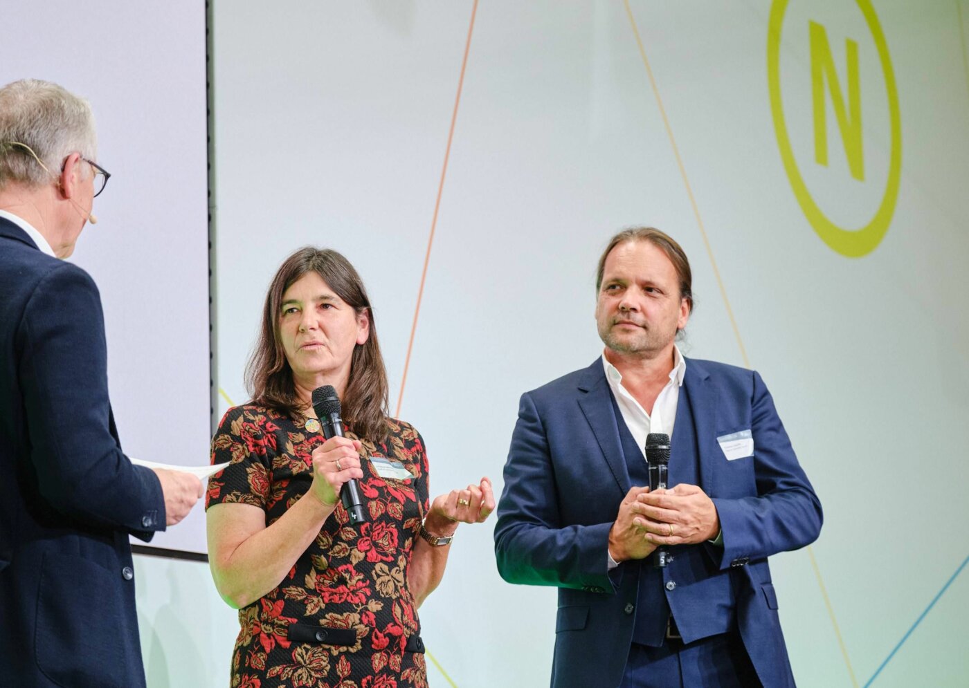 Auf der Bühne der 22. Jahreskonferenz des RNE wird ein Preis verliehen. RNE-Mitglied Dr. Werner Schnappauf spricht mit Johanna Köhnlein und Christian Lösche von HygCen, den beiden Gewinnern des Preises "Projekt Nachhaltigkeit".