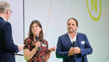 Auf der Bühne der 22. Jahreskonferenz des RNE wird ein Preis verliehen. RNE-Mitglied Dr. Werner Schnappauf spricht mit Johanna Köhnlein und Christian Lösche von HygCen, den beiden Gewinnern des Preises "Projekt Nachhaltigkeit".