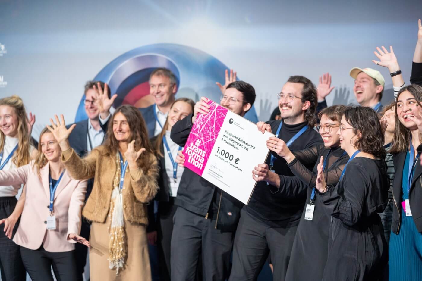 Die Gewinner von Wohnen+ stehen auf der Bühne bei der Verleihung des Deutschen Nachhaltigkeitspreises und halten ein Schild mit dem Preisgeld hoch.