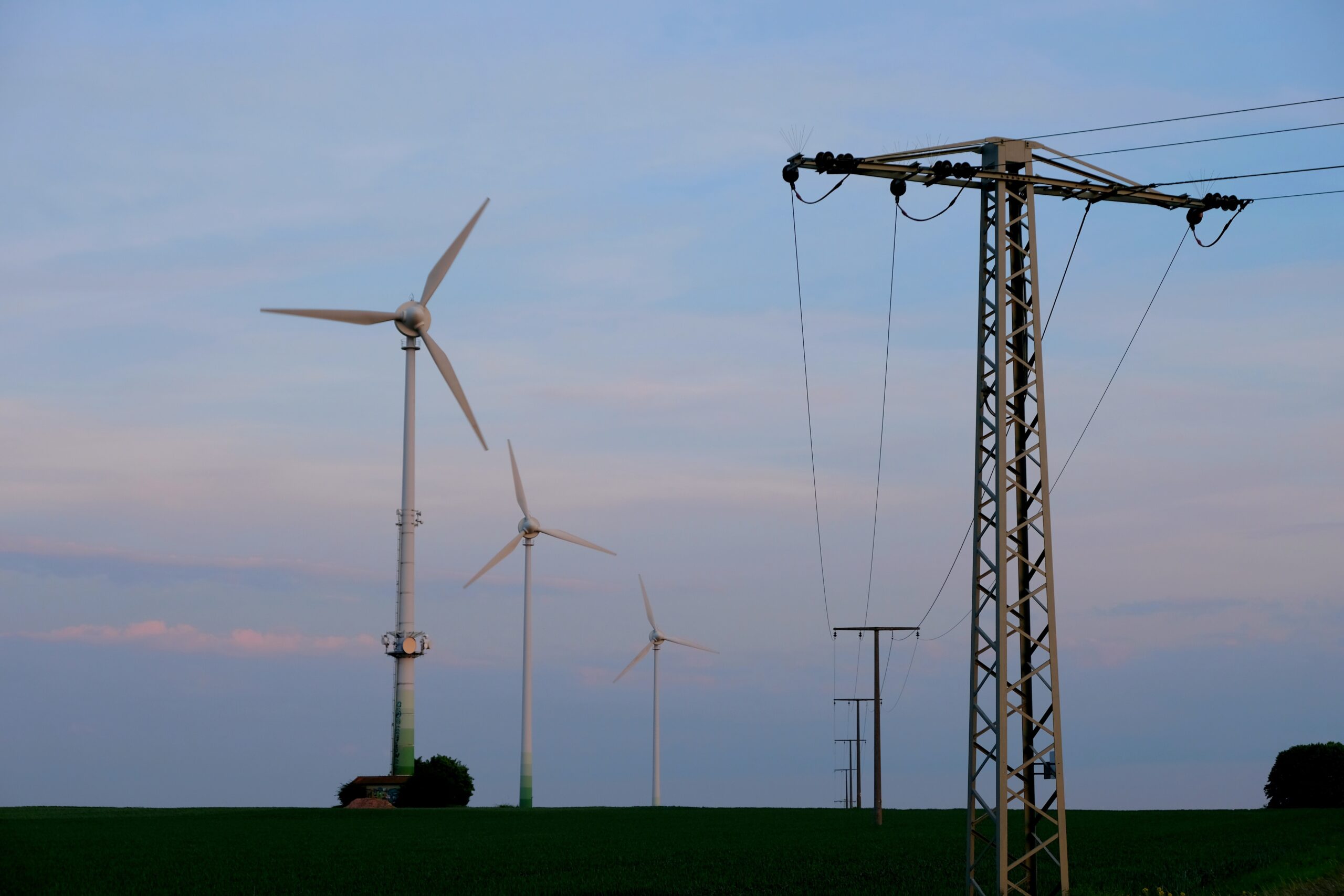 Windräder und Strommasten auf einer Freifläche in der Abenddämmerung